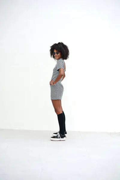 年轻的女人 留着非洲式的头发 站在白墙上摆着姿势 穿时髦休闲装的女孩 街上风格 大量的复制空间 免版税图库照片