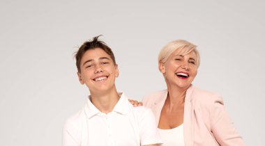 Neşeli genç çocuk açık gri stüdyo arka planında komik annesiyle poz veriyor ve bir sürü fotokopi alanı var. Kadın oğluyla eğleniyor. Anneler Günü konsepti