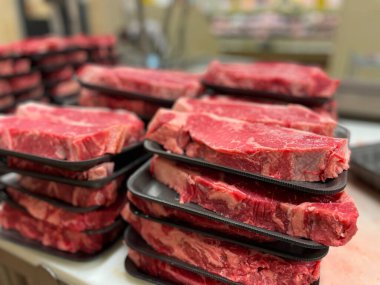 Bakkalda siyah tepsilerde kesilmiş çiğ biftekler yığılmış bulanık arka planda