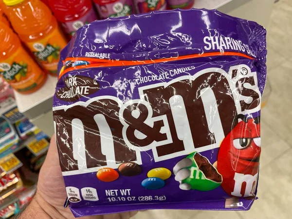 Grovetown, Ga USA - 02 17 23: Grocery store hand holding MM candy M and Ms purple bag
