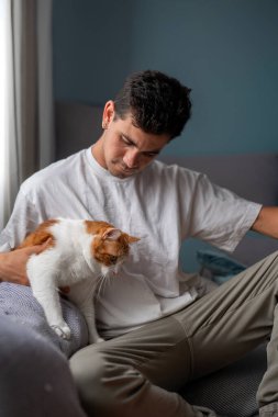 Genç adam oturma odasında kahverengi bir kediyle etkileşime girer.