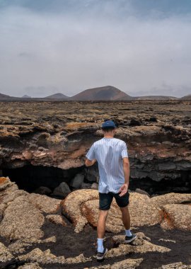 Genç adam Las Palomas Mağarası 'nın girişine bakıyor. Timanfaya Ulusal Parkı. Lanzarote. Kanarya Adaları