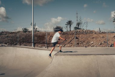 Genç adam güneşli bir günde kaykay parkında paten kayıyor.