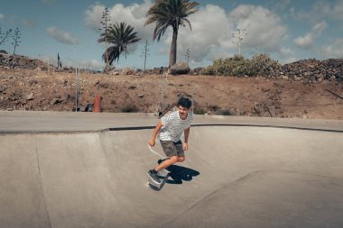 Genç adam güneşli bir günde kaykay parkında paten kayıyor.