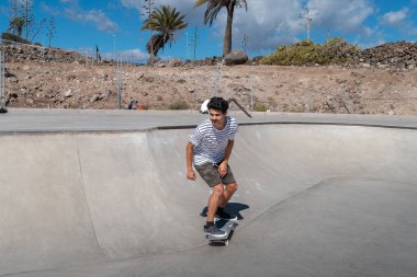 Genç adam güneşli bir günde kaykay parkında paten kayıyor.