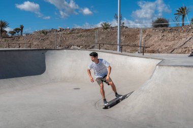 Genç adam güneşli bir günde kaykay parkında paten kayıyor.