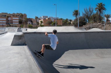 Genç adam güneşli bir günde kaykay parkında paten kayıyor.