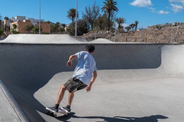 Genç adam güneşli bir günde kaykay parkında paten kayıyor.