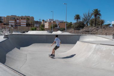 Genç adam güneşli bir günde kaykay parkında paten kayıyor.