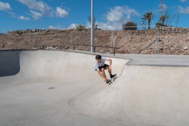 Genç adam güneşli bir günde kaykay parkında paten kayıyor.