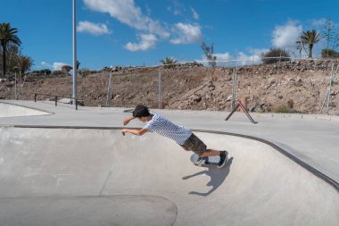 Genç adam güneşli bir günde kaykay parkında paten kayıyor.