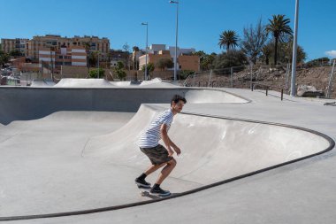 Genç adam güneşli bir günde kaykay parkında paten kayıyor.