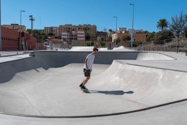 Genç adam güneşli bir günde kaykay parkında paten kayıyor.