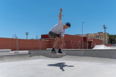 Genç adam güneşli bir günde kaykay parkında paten kayıyor.