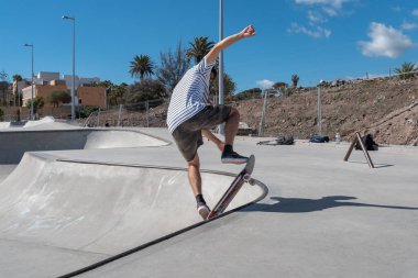 Genç adam güneşli bir günde kaykay parkında paten kayıyor.