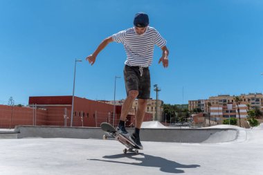 Genç adam güneşli bir günde kaykay parkında paten kayıyor.