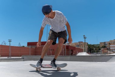 Genç adam güneşli bir günde kaykay parkında paten kayıyor.