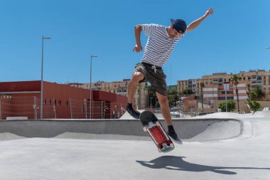 Genç adam güneşli bir günde kaykay parkında paten kayıyor.