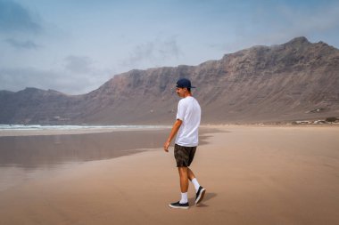 Genç adam Famara plajını ziyaret ediyor. Teg giyin. Lanzarote. Kanarya Adaları. İspanya