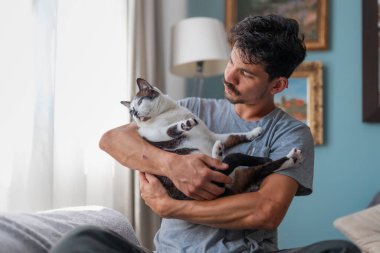 Genç adam evcil kediyle oturma odasında iletişim kuruyor.