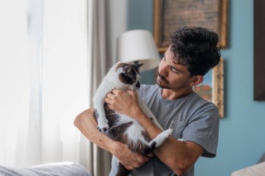 Genç adam evcil kediyle oturma odasında iletişim kuruyor.