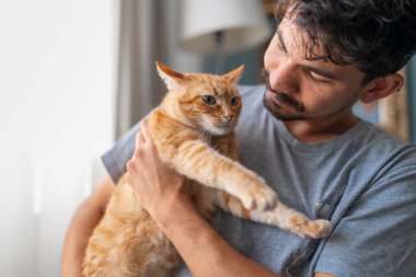 Genç adam evcil kediyle oturma odasında iletişim kuruyor.