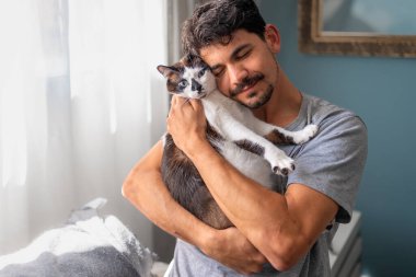 Genç adam evcil kediyle oturma odasında iletişim kuruyor.