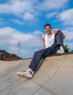 young man skater sitting on the edge of the bowl in a skate park clipart