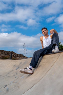 Genç kaykaycı bir kaykay parkında kasenin kenarında oturuyor.