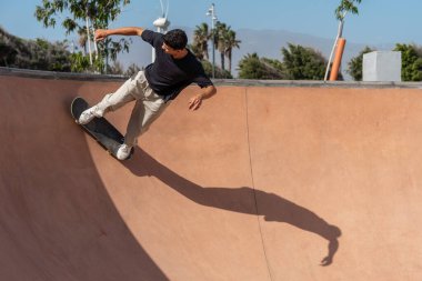Güneşli bir günde Arinaga kaykay parkında siyah tişört giyen genç bir kaykaycı.