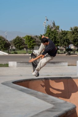 Güneşli bir günde Arinaga kaykay parkında siyah tişört giyen genç bir kaykaycı.