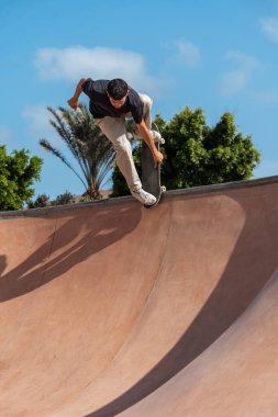 Güneşli bir günde Arinaga kaykay parkında siyah tişört giyen genç bir kaykaycı.