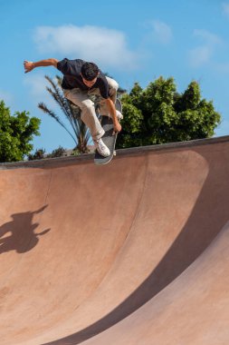 Güneşli bir günde Arinaga kaykay parkında siyah tişört giyen genç bir kaykaycı.