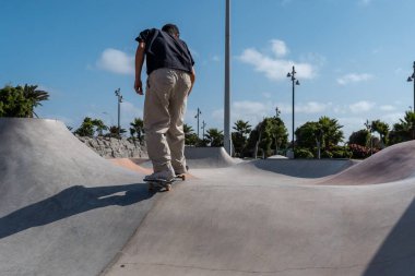 Güneşli bir günde Arinaga kaykay parkında siyah tişört giyen genç bir kaykaycı.