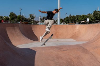 Güneşli bir günde Arinaga kaykay parkında siyah tişört giyen genç bir kaykaycı.