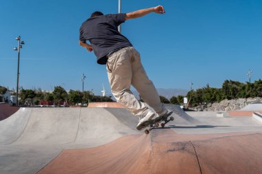 Güneşli bir günde kaykay parkında siyah tişört giyen genç bir kaykaycı.