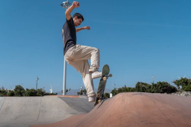 Güneşli bir günde kaykay parkında siyah tişört giyen genç bir kaykaycı.
