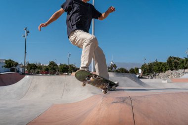 Güneşli bir günde kaykay parkında siyah tişört giyen genç bir kaykaycı.