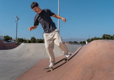 Güneşli bir günde kaykay parkında siyah tişört giyen genç bir kaykaycı.