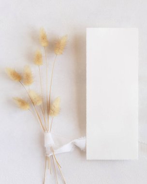 İpek kurdelelerin yanındaki boş kart ve kurutulmuş tavşanın kuyruğundaki çim beyaz, maket. Boho romantik sahnesi ve dikey kart. Bohem ya da doğaya yakın selamlama ya da düğün davetiyesi