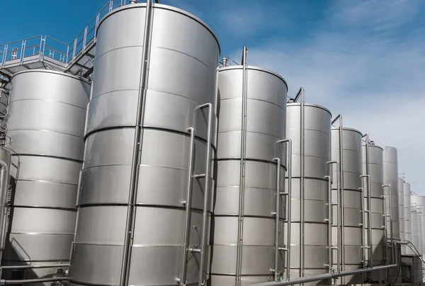 A row of steel wine tanks for wine fermentation at a modern winery. Large brewery silos typically used for storing barley or fermeted beer against blue sk