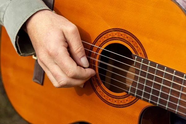 Male hands playing acoustic guitar, close up.  Practicing in playing guitar. Teacher is giving guitar lesson. Natural light lifestyle scene