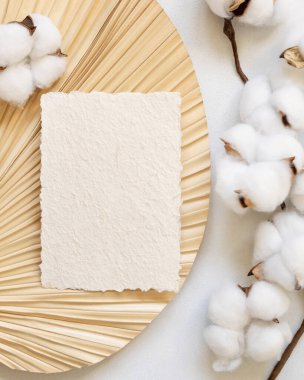 Pamuk çiçekli kurutulmuş palmiye yaprağının üzerinde boş el yapımı kağıt kart, üst görünüm, maket. Dikey kartla romantik bir sahne. Bohem Pastel selamlama ya da düğün davetiyesi