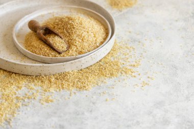 Pile of Dry uncooked bulgur wheat grain with a scoop on a plate close up, copy space. Vegetarian and Vegan, Mediterranean and Middle Eastern cuisine. Healthy lifestyle