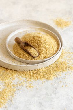 Pile of Dry uncooked bulgur wheat grain with a scoop on a plate close up, copy space. Vegetarian and Vegan, Mediterranean and Middle Eastern cuisine. Healthy lifestyle