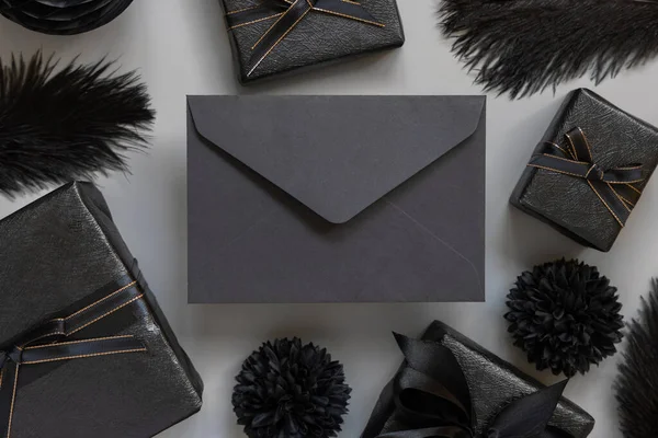 Černá Obálka Mezi Zabalenými Dárkovými Krabicemi Černými Papírovými Květinami Peřím — Stock fotografie