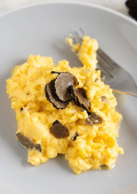 Scrambled eggs with sliced fresh black truffles from Italy served in a plate close up. Italian cousine, gourmet breakfast 