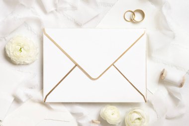 Krem güllerin yanında boş bir zarf, beyaz ipek kurdeleler ve alyanslar üst manzara, düğün modeli. Dikey kart ve pastel çiçeklerin düz olduğu romantik bir sahne. Sevgililer Günü, Bahar veya Anneler Günü konsepti