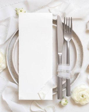 Krem güllerin yanında kart ve beyaz ipek kurdeleler olan düğün masası, üst manzara, maket. Dikey menü kartı ve pastel çiçeklerle romantik bir sahne. Sevgililer Günü, Bahar veya Anneler Günü konsepti