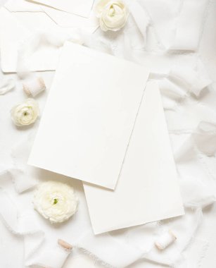 Krem güllerin yanındaki boş kartlar ve beyaz ipek kurdeleler üst manzara, düğün modeli. Dikey kartlar ve pastel çiçeklerin düz olduğu romantik bir sahne. Sevgililer Günü, Bahar veya Anneler Günü konsepti